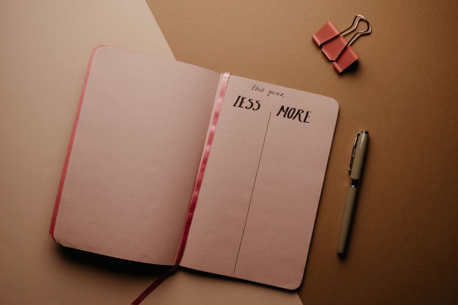 Open journal with 'less' and 'more' columns beside a pen, ready for goal planning