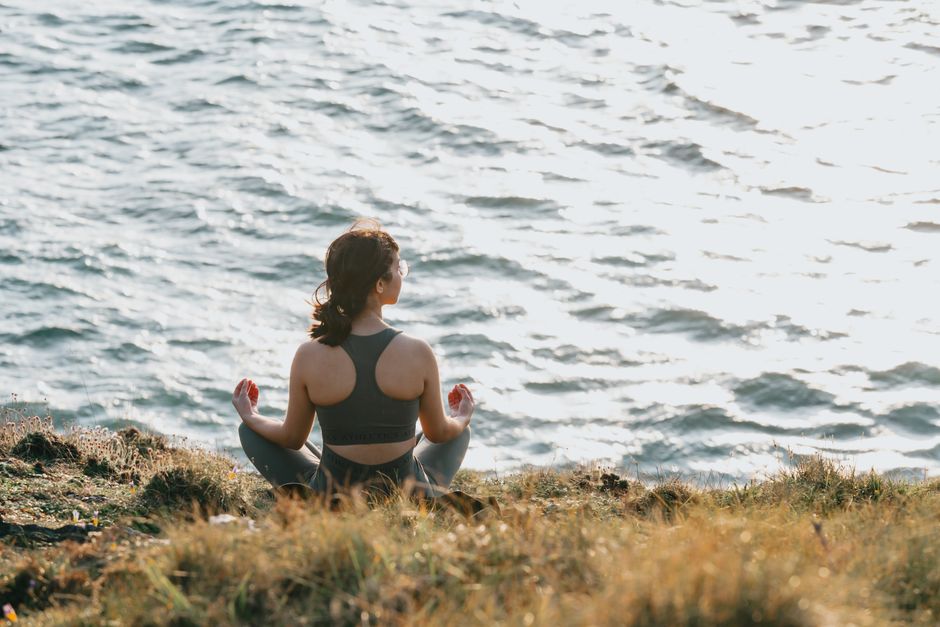Person meditating cross-legged on a grassy bluff at the water's edge